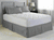 A neatly made bed with a Spring Air Illuna Plush Comfort Mattress Pad, gray bedskirt, and matching pillows in a serene bedroom with a white and gray color scheme, complemented by soft