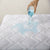 A person pouring a liquid onto a Down Etc. Lily-Pad Waterproof Mattress Pad.