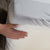 A person is holding a Protect-A-Bed Premium Mattress Protector on a bed.