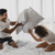 A man and woman having a pillow fight on a bed filled with Envirosleep Dream Memories Memorelle Fiber Fill Pillows by Manchester Mills.