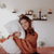 A woman holding a Hollander Holiday Inn® Polyester Pillow | Firm Support on her bed.