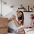 A woman sitting on a bed with pillows filled with Temperloft Down/Down Alternative and a box, featured at many hotels by Sysco Guest Supply.